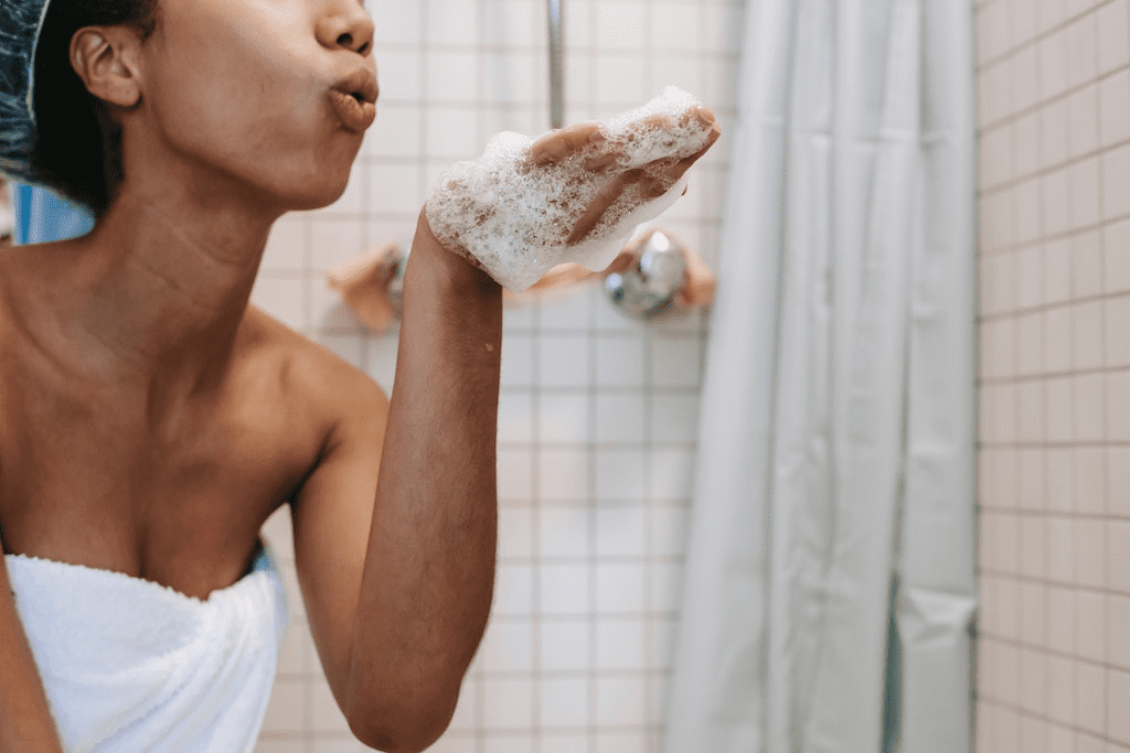 Mulher aplicando shampoo para limpeza profunda em seu couro cabeludo no banheiro.