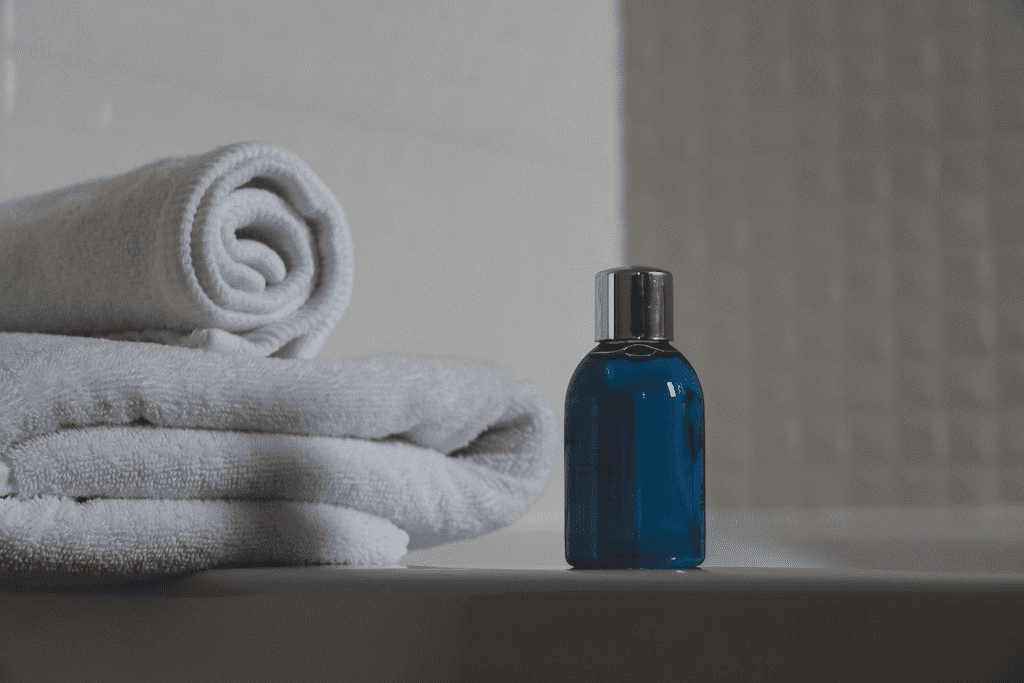 Frasco de sabonete líquido azul ao lado de toalha branca no banheiro
