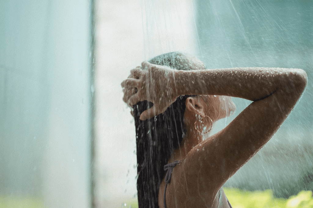 Jovem mulher lavando o cabelo no chuveiro.