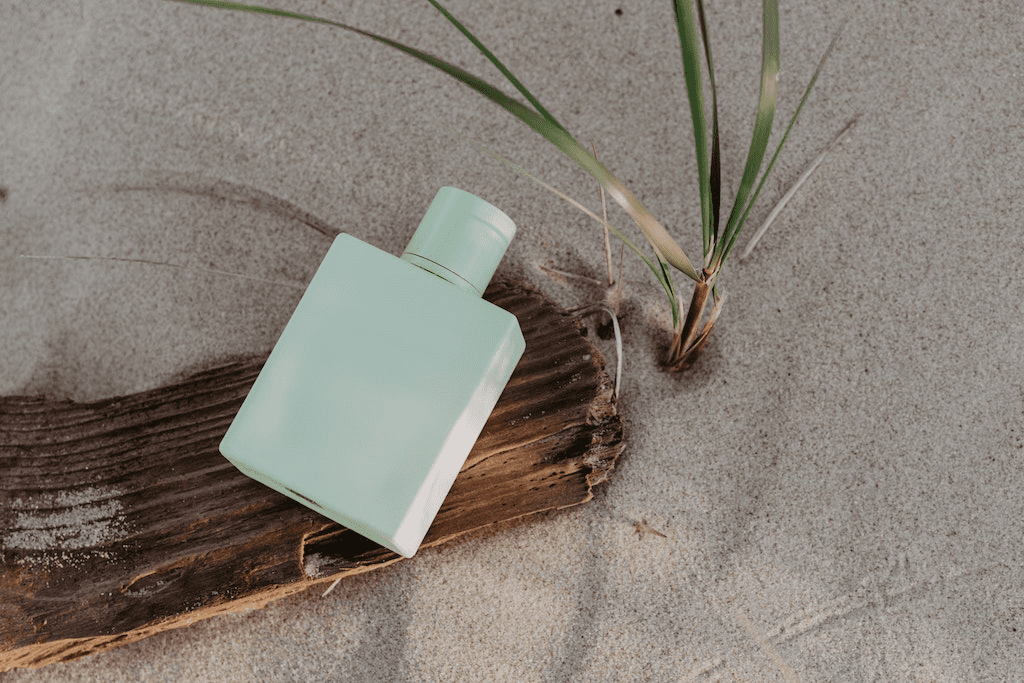 Garrafa de perfume verde sobre superfície de madeira na praia.