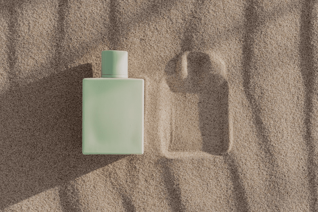 Frasco de desodorante colônia na areia representando fixação e aroma duradouro.
