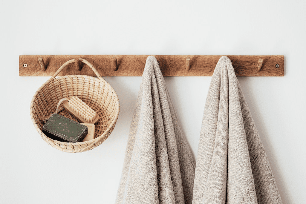 Cabide de madeira com toalhas e cesta com produtos de banho.
