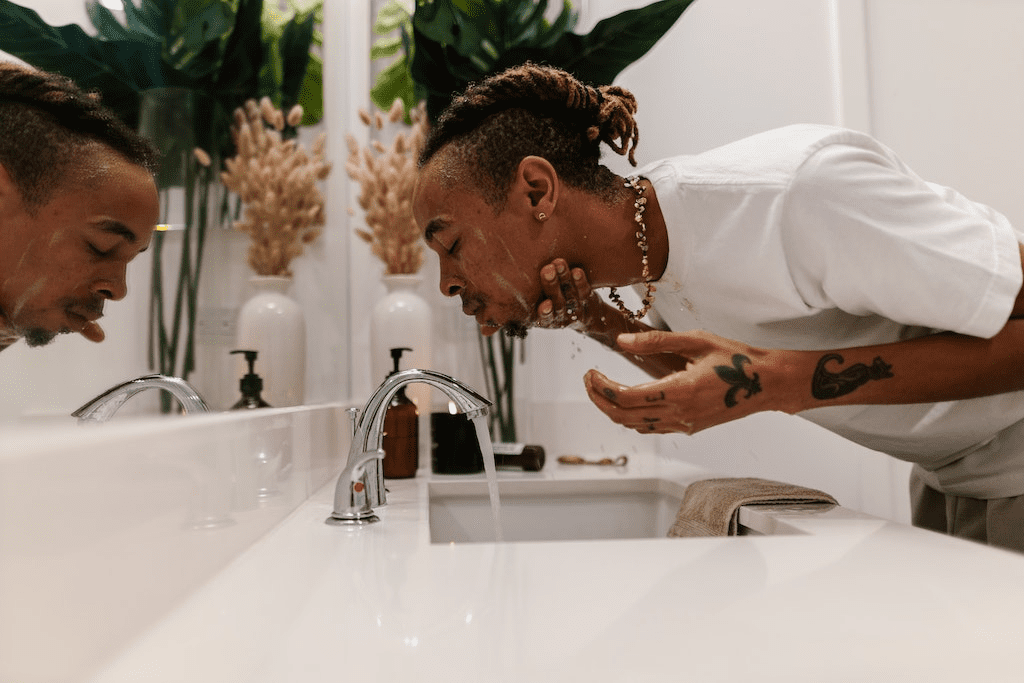 Homem lavando o rosto no banheiro com cleansing oil.